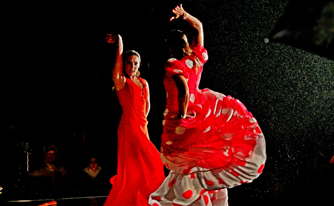 Two flamenco dancers in red in a dramatic pose against a black background.