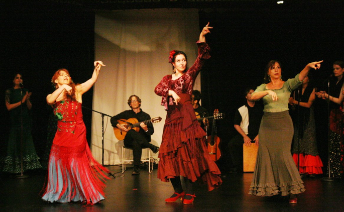 Three dancers performing on stage with musicians in the background.